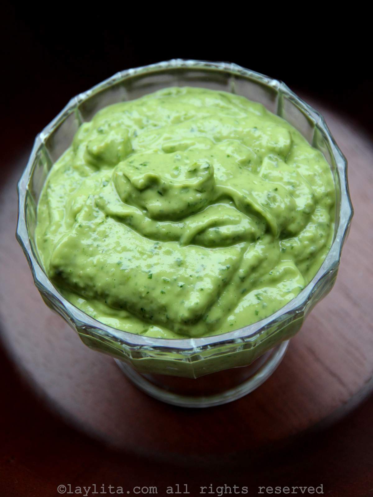 Overhead shot of avocado sauce in a glass bowl on a wood background