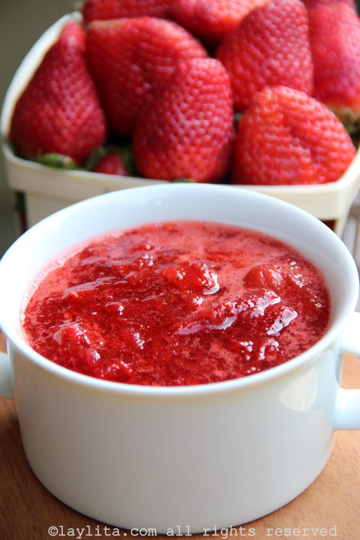 Closeup of a bowl of strawberry sauce with a container of fresh strawberries in the background
