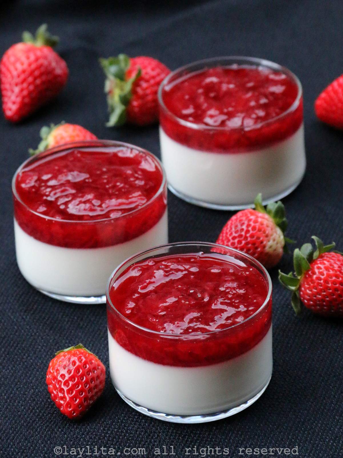 Three dessert cups filled with panna cotta and topped with fresh strawberry topping sauce