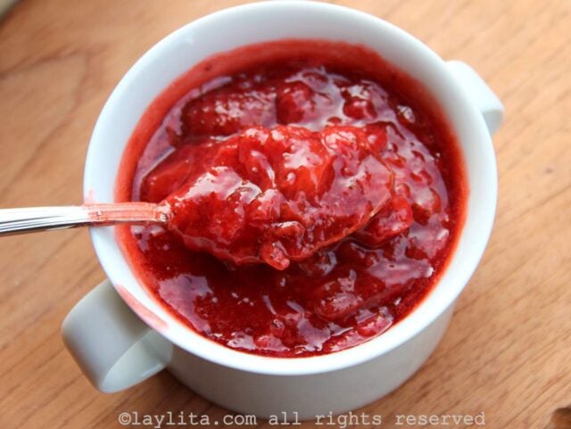 A bowl of strawberry sauce with a spoon showing some of the sauce