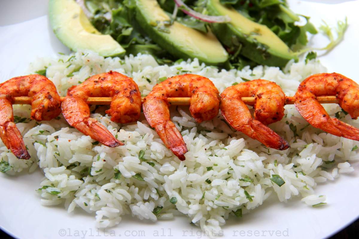 A plate with lime cilantro rice topped with a grilled shrimp skewer and a green salad with avocado slices in the back of the plate