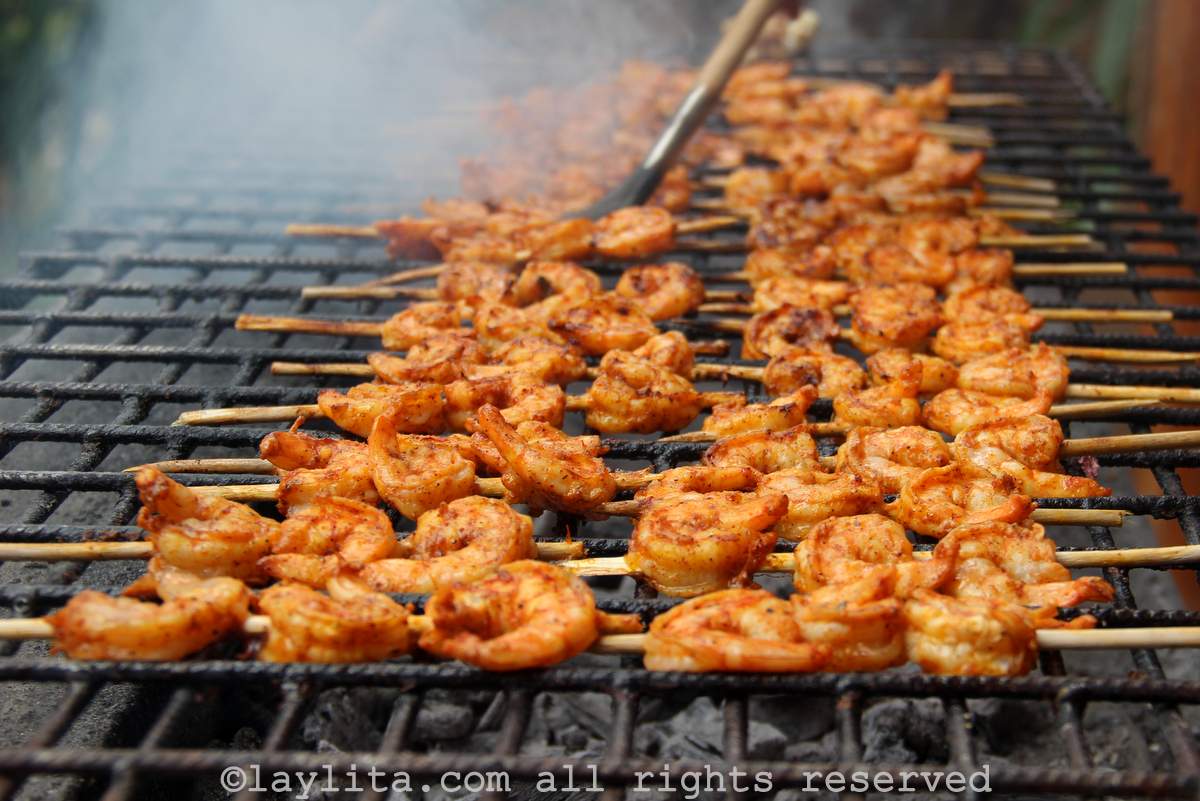 Several small skewers with shrimp on them being grilled on a rustic charcoal grill