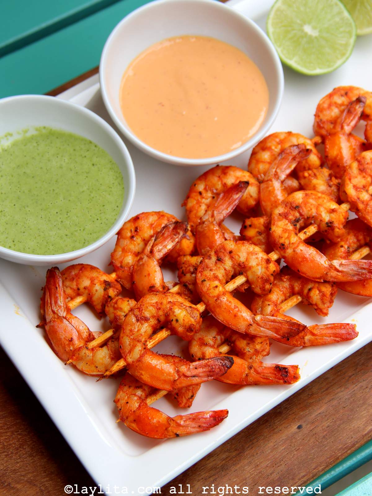 Overhead shot of a white platter with grilled shrimp skewers next to two bowls with dipping sauces