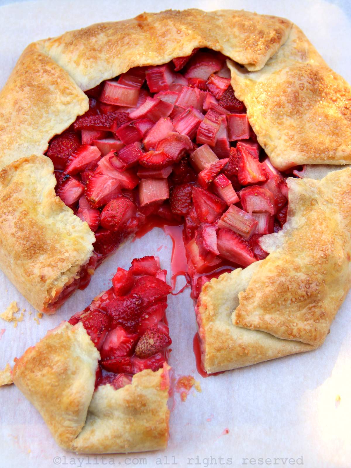 Vertical shot of a rhubarb strawberry galette on a piece of parchment paper with a slice cut out of the galette
