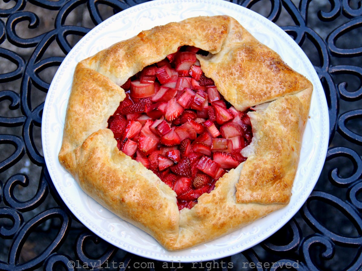A rustic rhubarb and strawberry galette tart on a white plate on top of a metal table