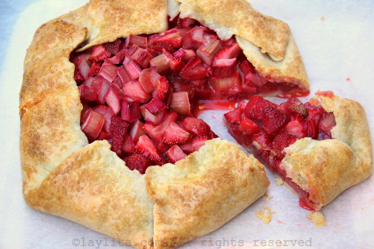 View of a rhubarb strawberry galette on a piece of parchment paper with a slice cut out of the galette