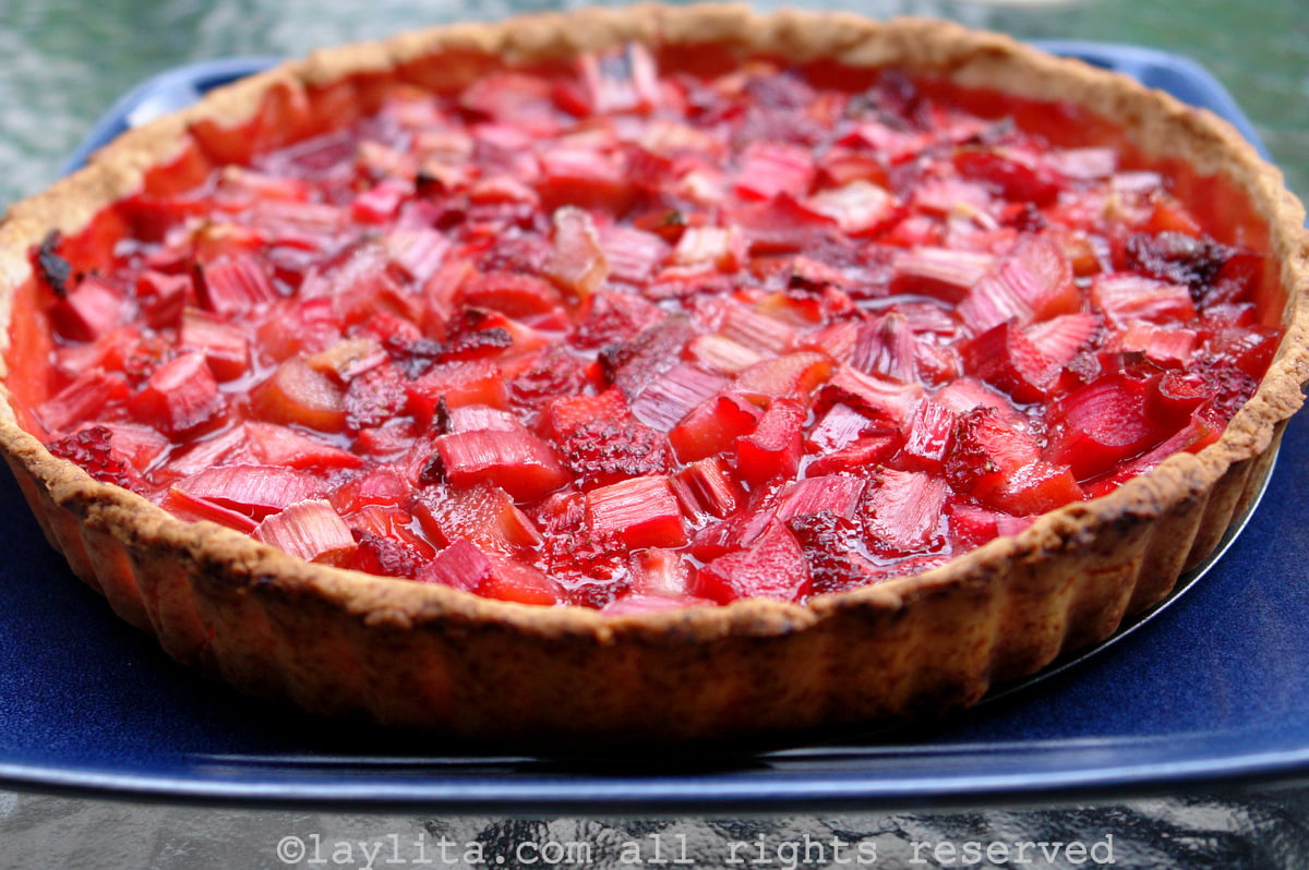 A rhubarb strawberru tart on a blue palte on a glass table