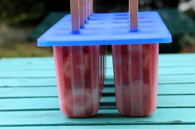 Place the reserved sliced strawberries on the edges of the molds, pour in the puree, cover and add the popsicle sticks.