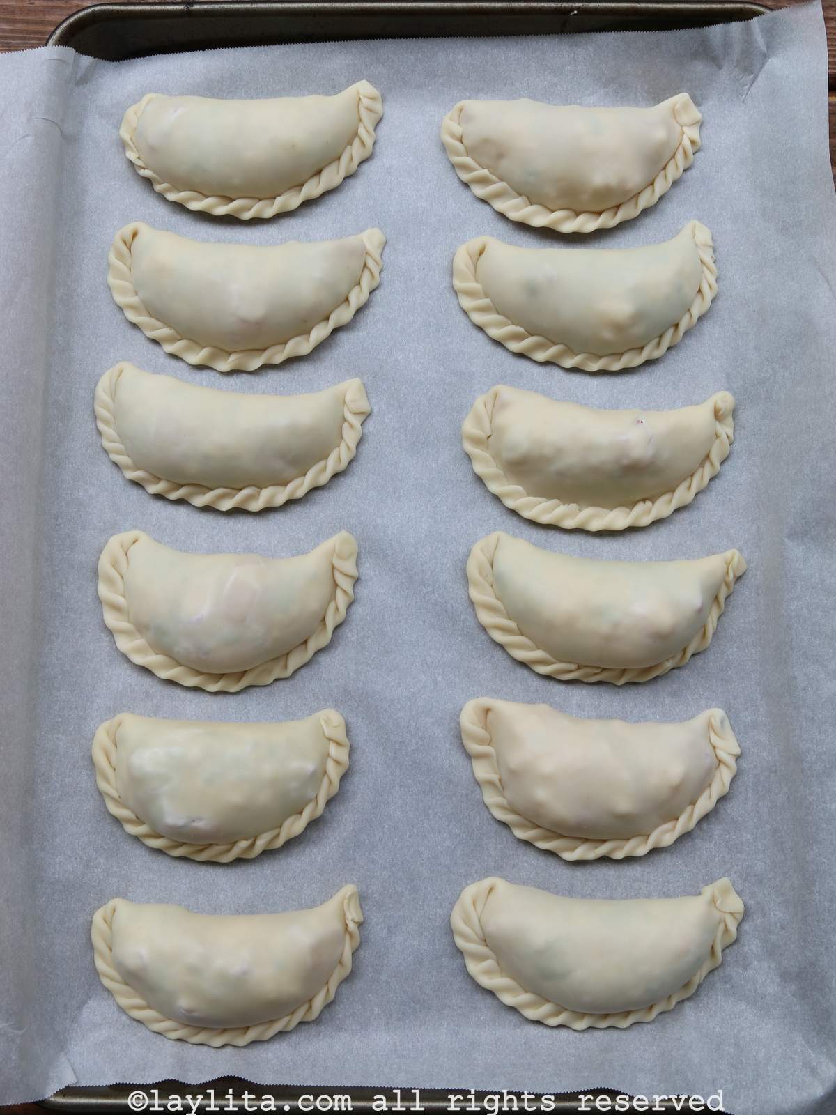 Overhead shot of twelve unbaked empanadas on a baking sheet lined with parchment paper