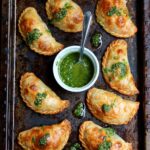 Overhead shot of caprese empanadas topped with basil garlic oil sauce with more sauce in a ramekin.