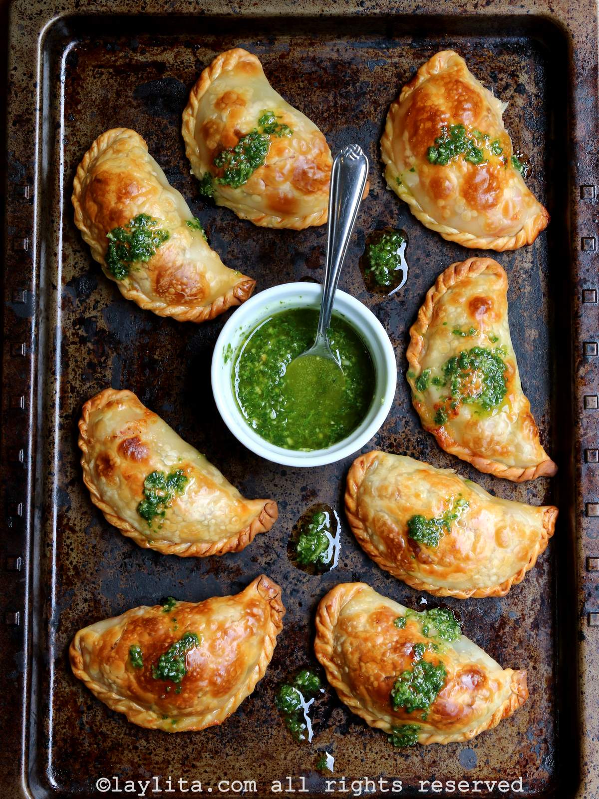Tomato mozzarella empanadas with basil garlic sauce Overhead shot of caprese empanadas topped with basil garlic oil sauce with more sauce in a ramekin.
