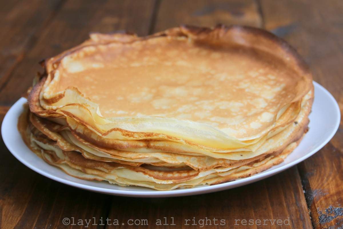 A white plate with a stack of French crepes on a wood table