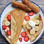 White and blue plate with crepes filled with strawberries and bananas