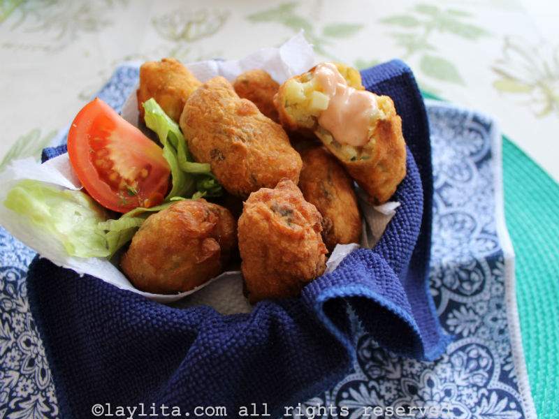 Brazilian cassava fritters in a bowl lined with blue towel and with some salsa rosada on top of one of the fritters