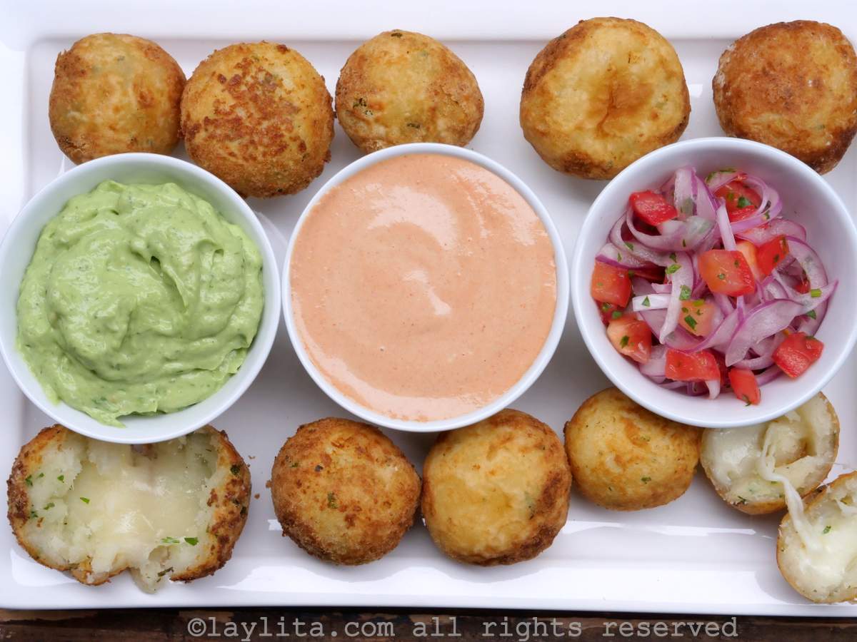 Fried yuca balls filled with cheese, on a white platter with dipping sauces