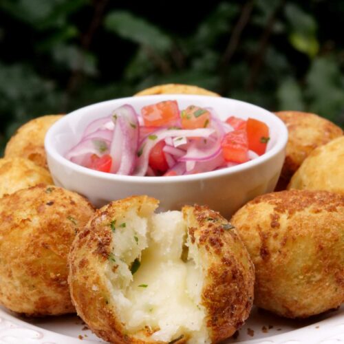 Fried yuca balls stuffed with cheese on a white plate with a bowl of tomato onion salsa in the middle of the plate