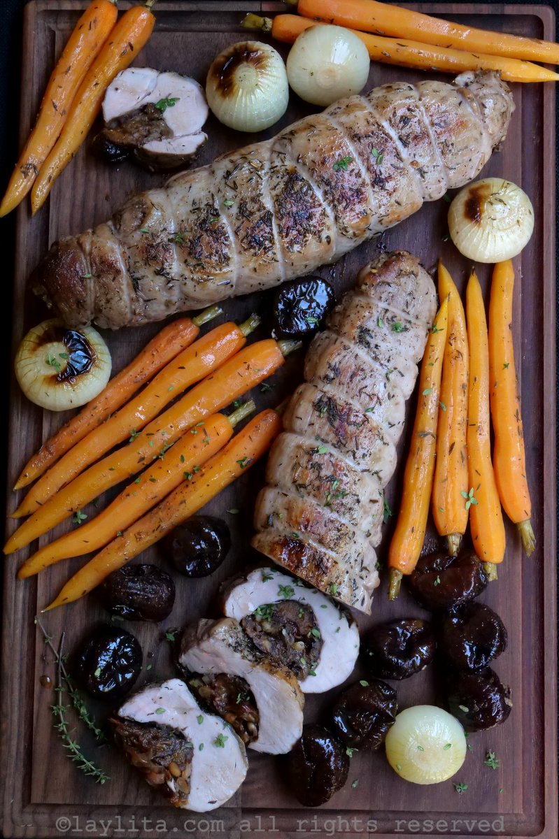 Overhead shot of two stuffed pork tenderloins with prunes, shallots and pine nuts on cutting board with additional roasted vegetables