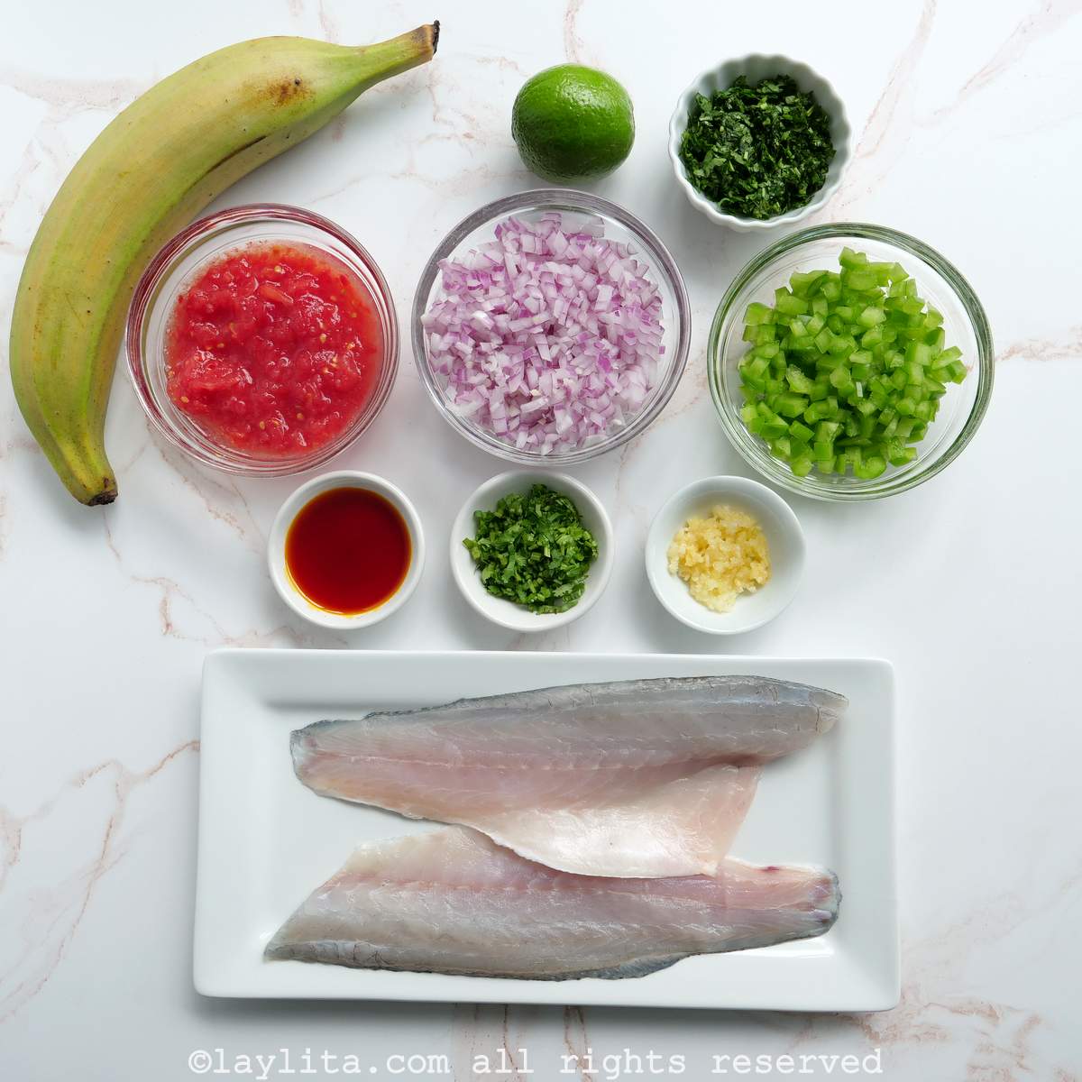 Ingredients for Ecuadorian sudado de pescado or fish stew with plantains: Green plantain, fish filets, grated tomatoes, diced red onions, diced green bell peppers, diced cilantro, lime, crushed garlic, achiote oil