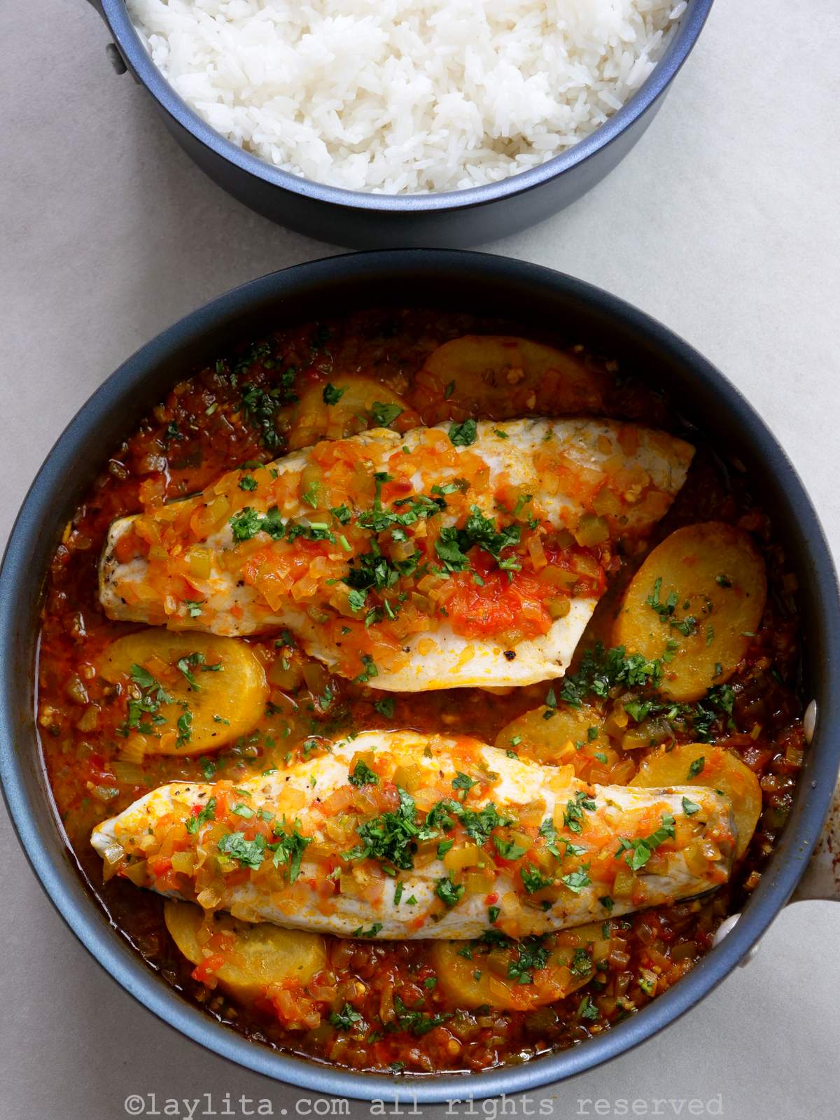Fish stew with plantains in a skillet next to a pot of cooked white rice.
