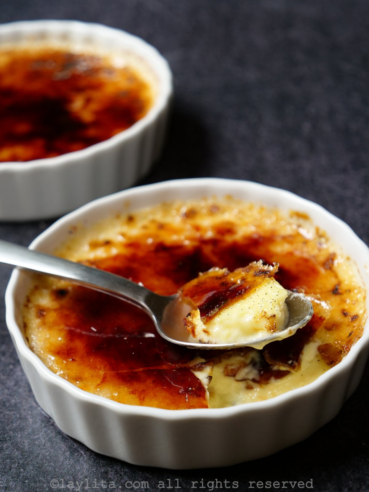 Creme brulee in two ramekins with a spoon in one of them, taking out a bite.