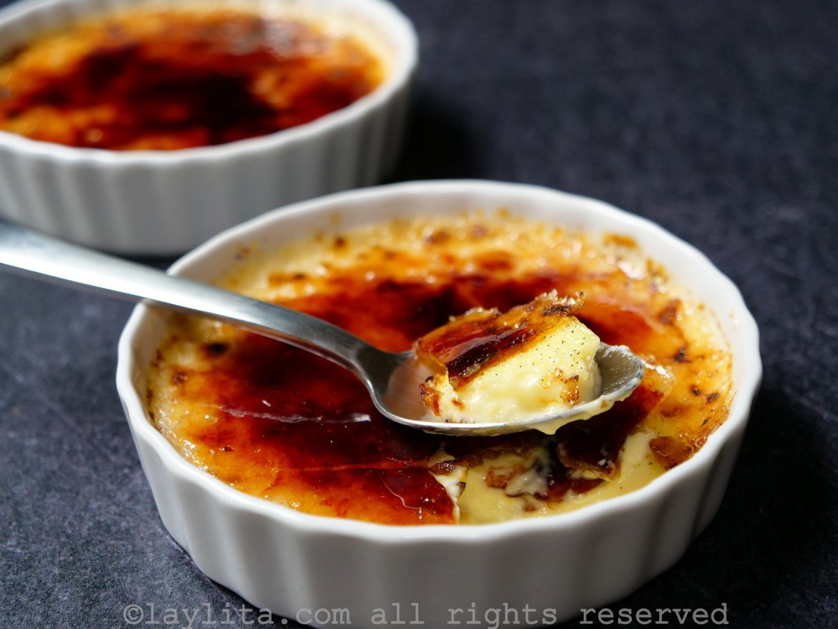 Close up shot of ramekin of creme brulee with a spoon taking a bite from it.