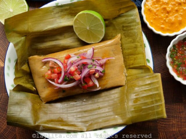 Overhead shot of bollos de pescado served on a plate topped with peanut sauce and sliced onions and tomatoes with sauce and tomato salad on the side.