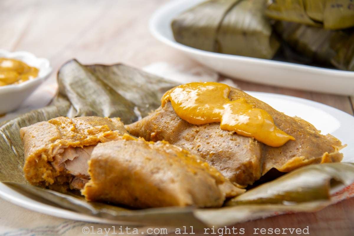 Side view of two bollos served on a plate with one of the opened to show the fish in the middle and peanut sauce on top.