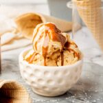 White bowl filled with caramel ice cream with some cones in the background.