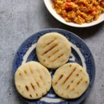 Overhead shot of three arepas on a plate next to a plate of scrambled eggs.