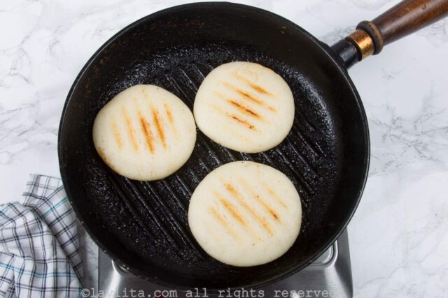 Overhead shot of three arepas in a cast iron griddle