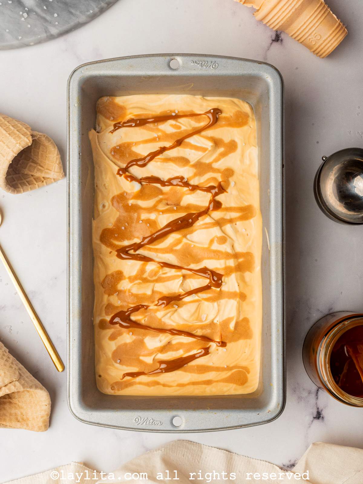 Salted caramel ice cream in a metal loaf pan with empty cones on the side.