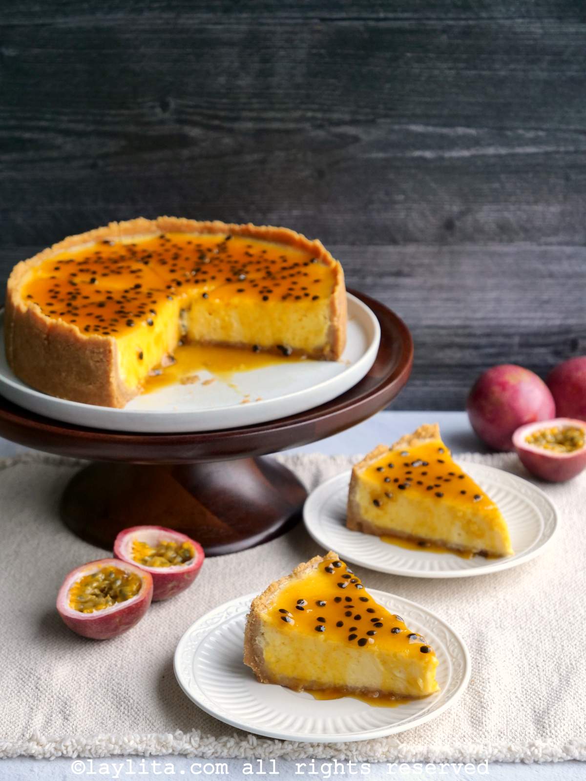 Passion fruit cheesecake on a plate with two slices missing and passion fruit halves in the background.