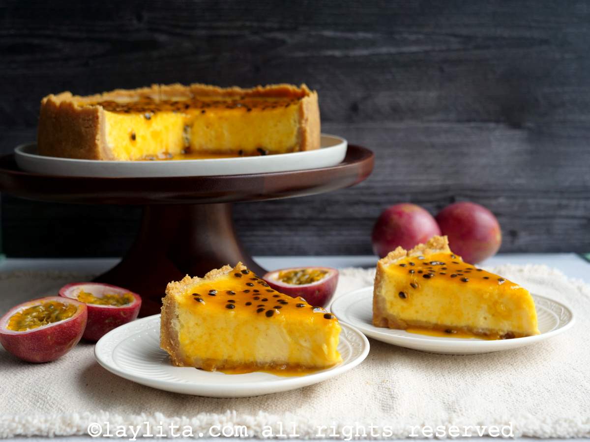 Two slices of passion fruit cheesecake on plates with the whole cheesecake on a cake platter in the background.