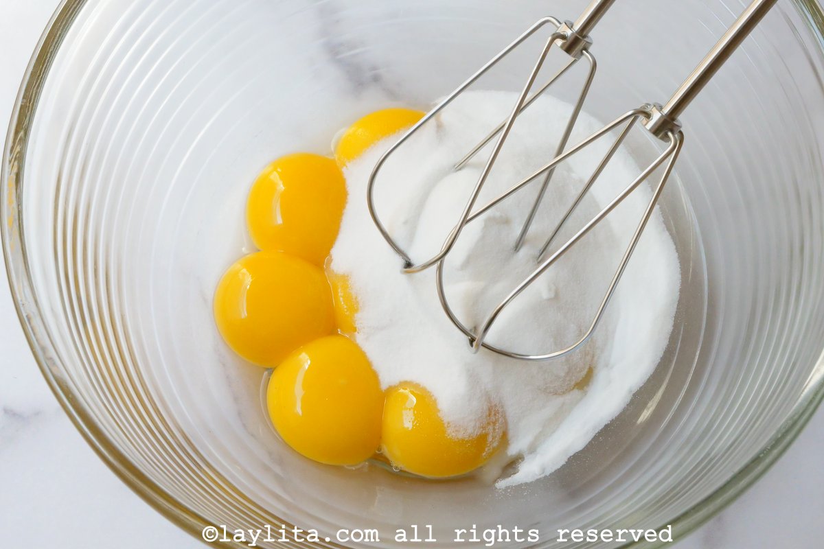 Egg yolks and sugar in a glass mixing bowl with an electric mixer.