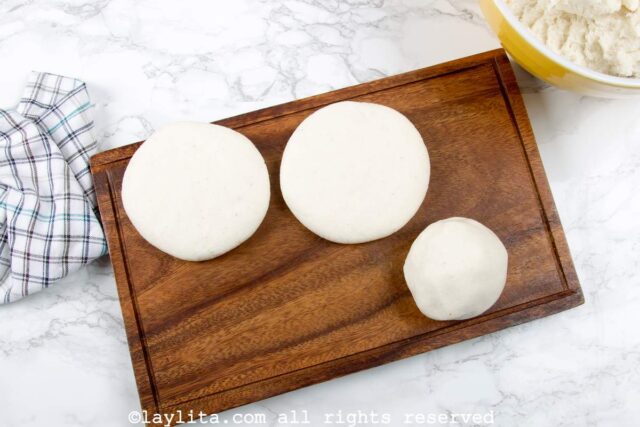 A board with two arepa patties and one arepa ball