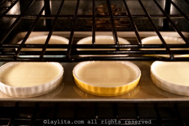 Ramekins of creme brulee in a baking dish slightly filled with water baking in the oven.