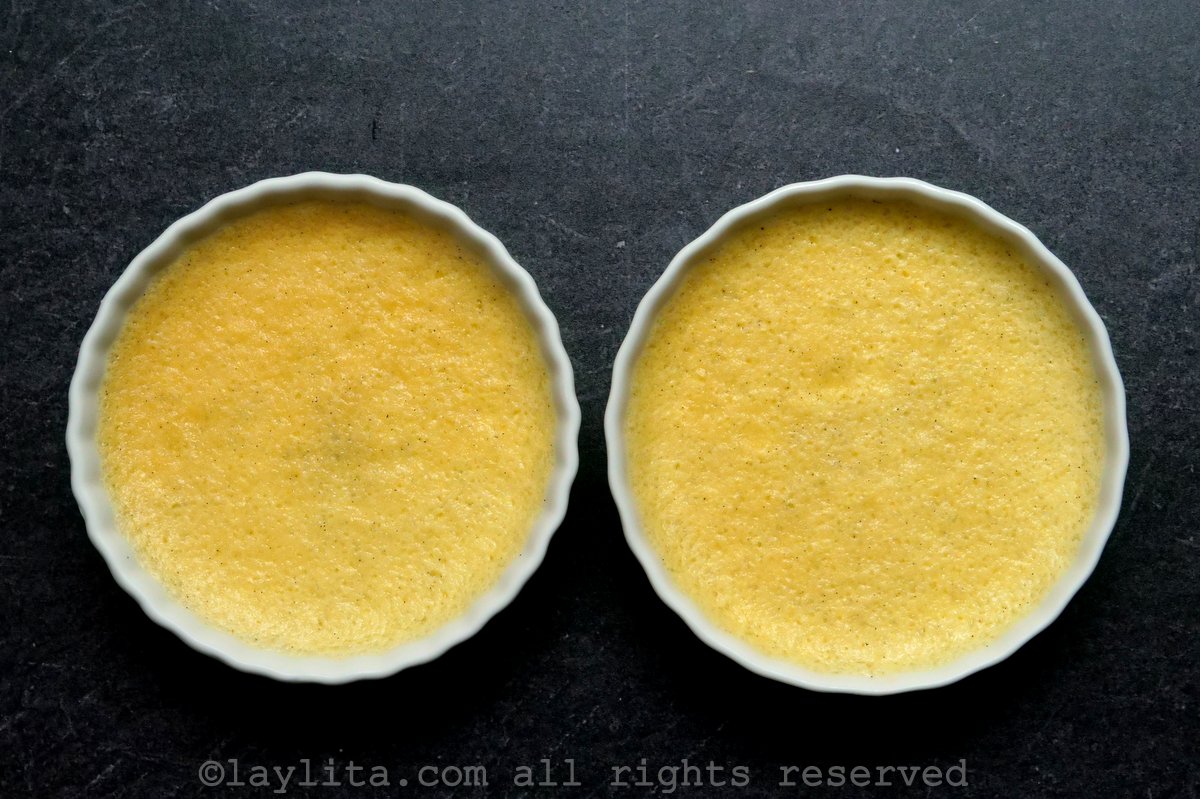 Two ramekins of creme brulee with sugar on top and a torch starting to burn the sugar