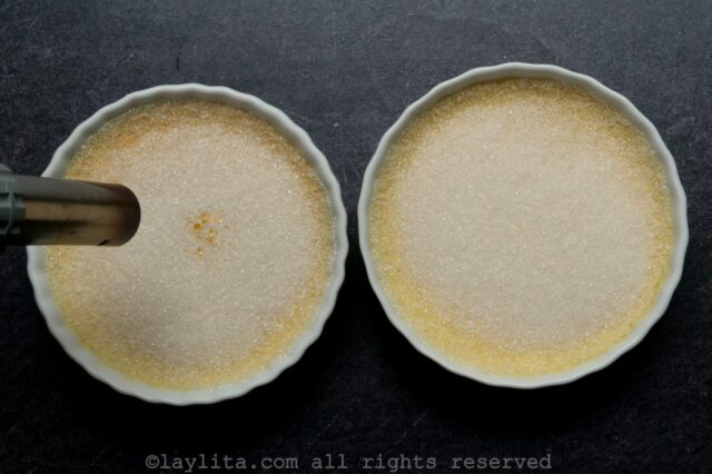 Two ramekins of creme brulee with burnt sugar layers on top.