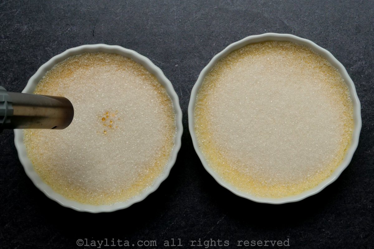Two ramekins of creme brulee with burnt sugar layers on top.