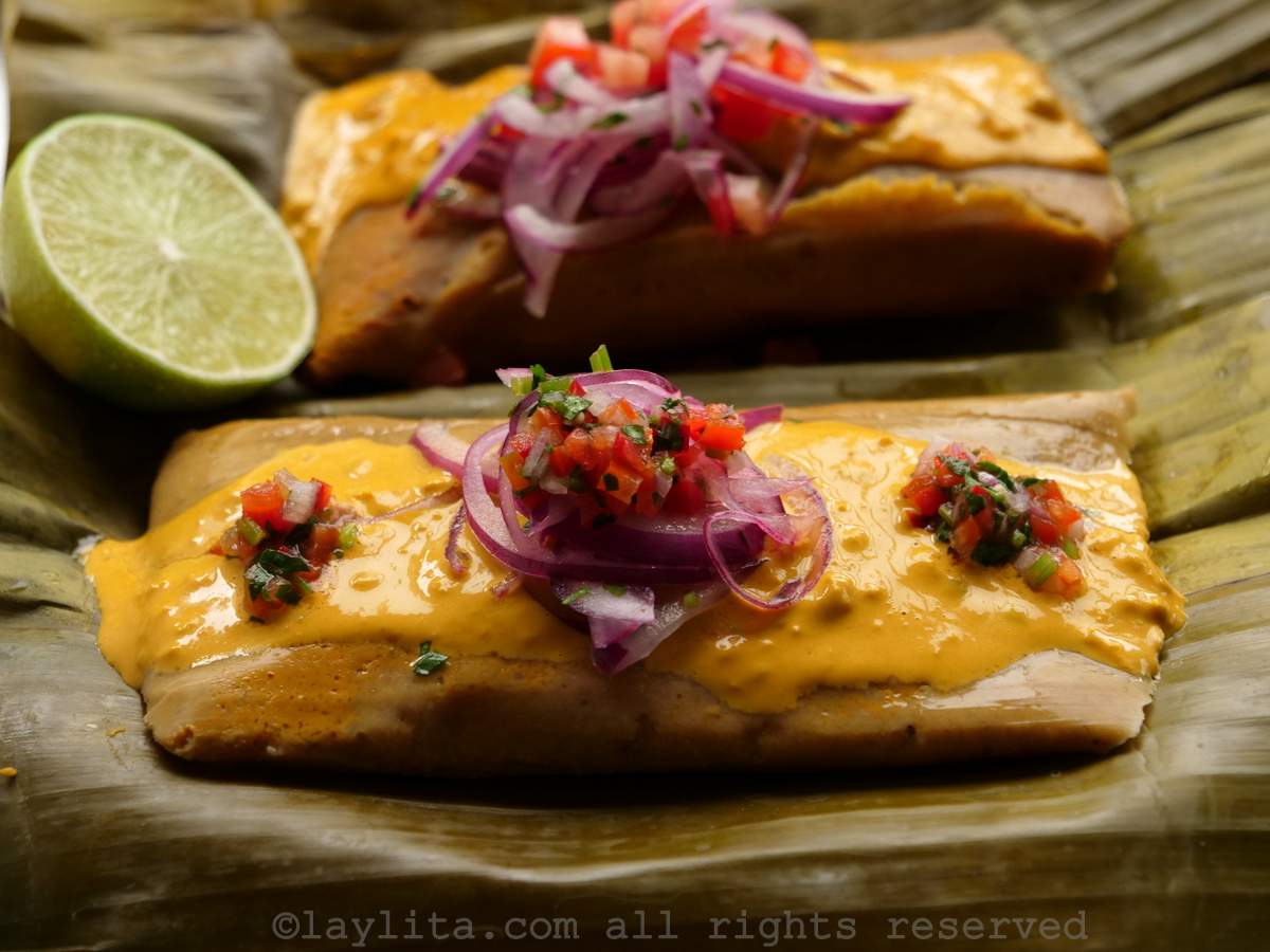 Photo of two bollos served on a plantain leaf topped with sliced onions, hot sauce, and a lime wedge. 