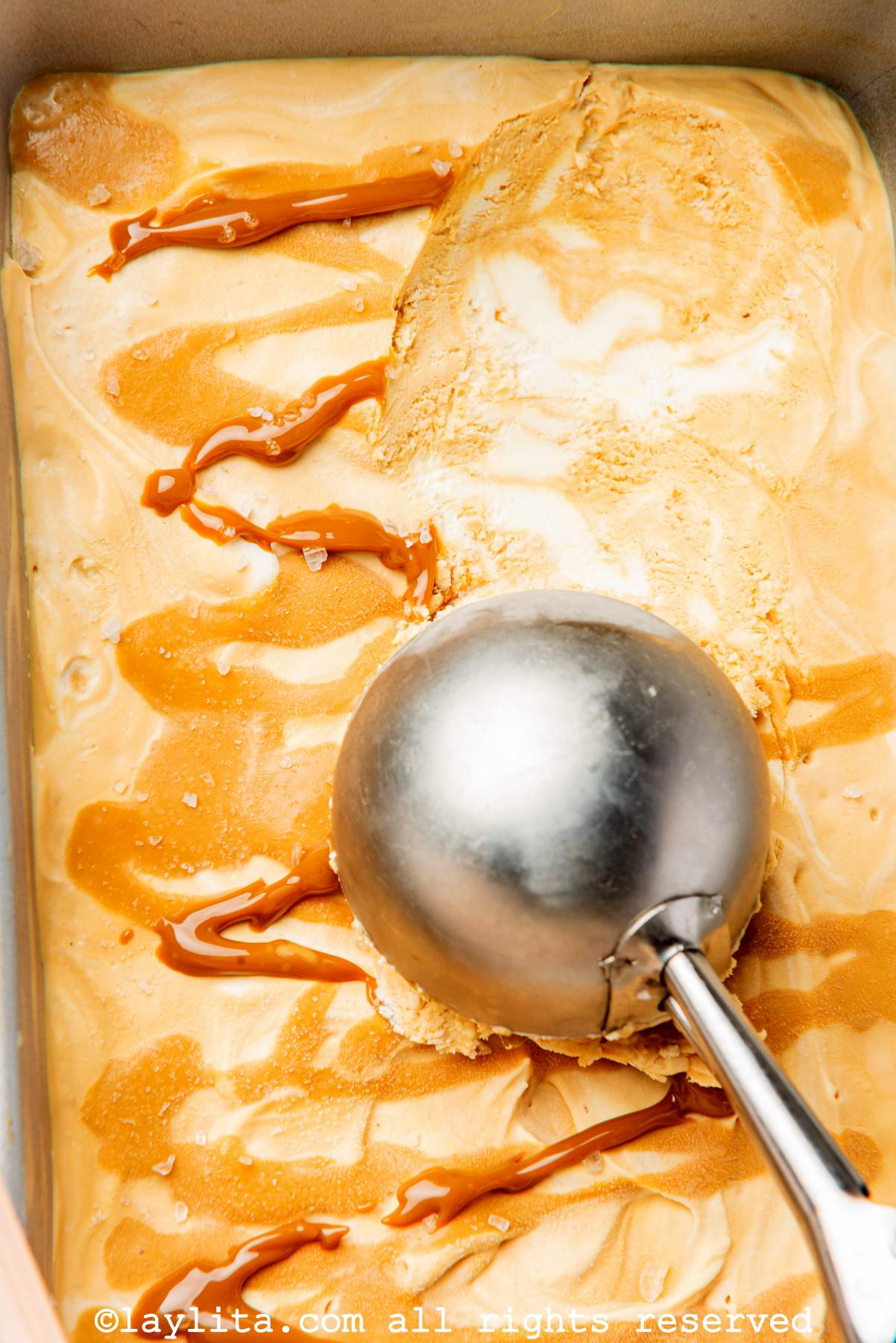 Close up of caramel ice cream in a loaf pan with an ice cream scoop scooping up some.