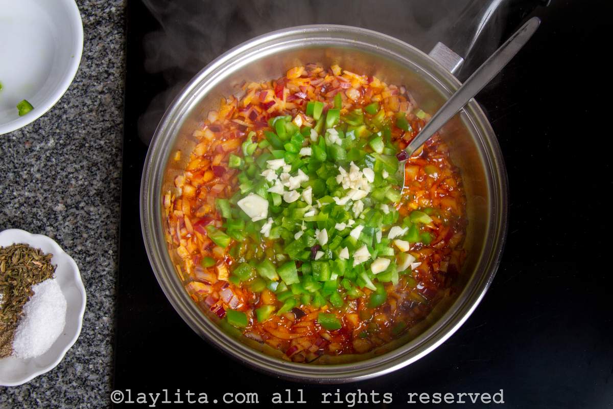 Onions, green peppers and garlic being cooked in a pot with achiote.