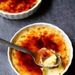 Creme brulee in two ramekins with a spoon in one of them, taking out a bite.