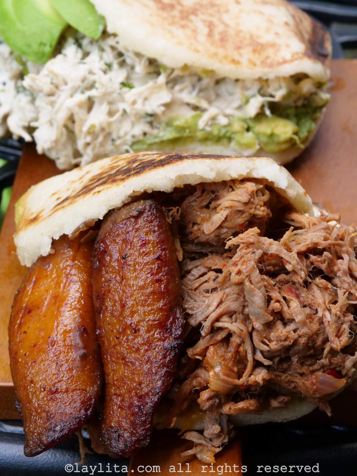 A board with Venezuelan arepas, one filled with shredded beef and ripe plantains, the other filled with chicken avocado salad