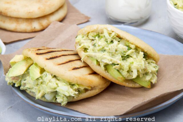 Two arepas filled with chicken avocado salad on a plate on a kitchen counter.