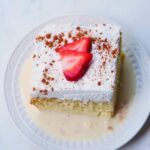 Slice of tres leches cake on a plate with strawberries on top.