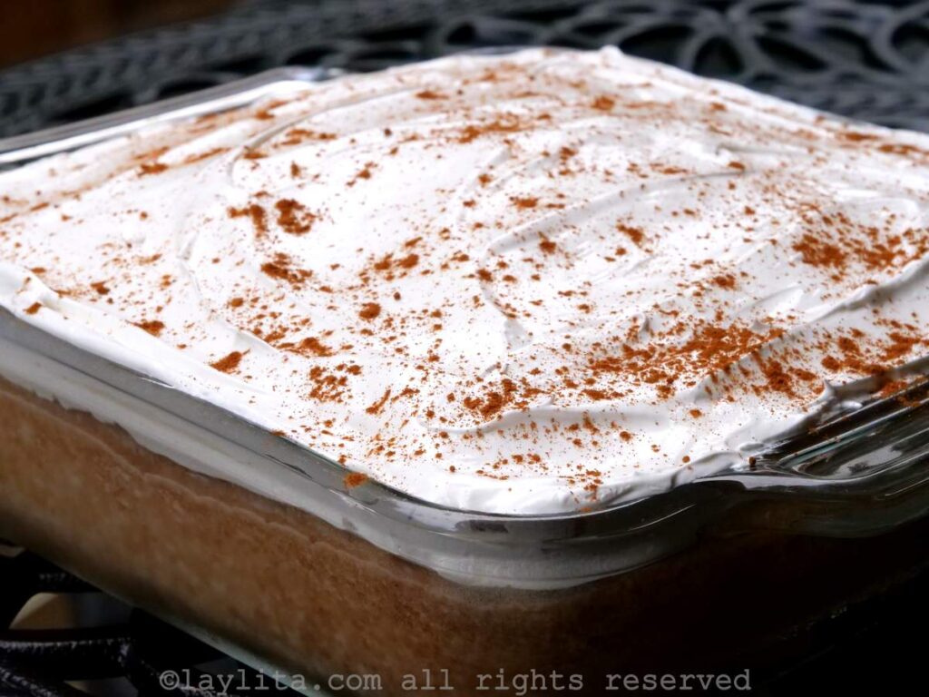 Side view of a tres leches cake in a glass cake pan on a table outside.