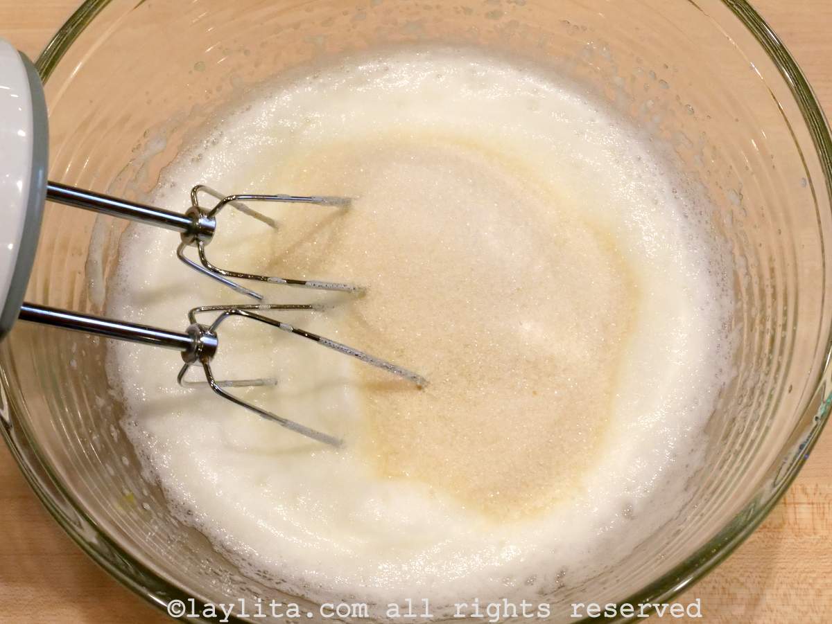 Sugar added to whipped egg whites in a bowl.