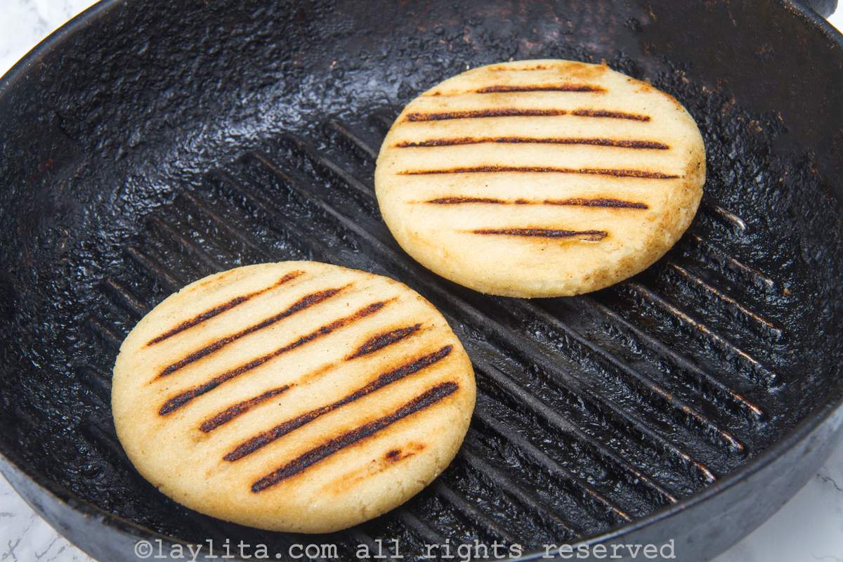 Arepas cooking in a cast iron skillet with grill marks on them.