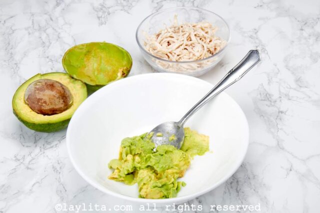 Avocados being smashed in a white bowl.
